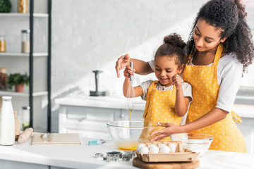 african american mother and daughter whisking eggs for dough in kitchen - Powered by Adobe