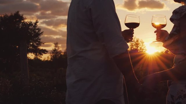 Romantic couple holding hands clink glasses with wine at sunset. - Powered by Adobe
