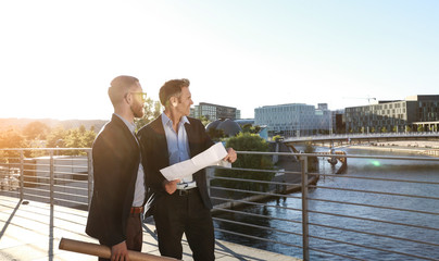 Two architects with blueprint standing on a bridge in the city