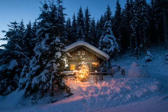 Illuminated wooden house with snowman and Christmas tree on snowy landscape