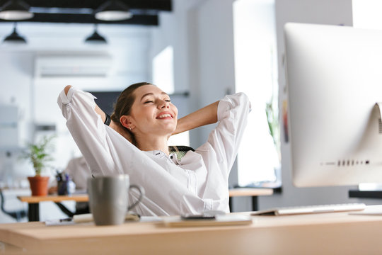 Happy young woman dressed in shirt sitting at her workplace