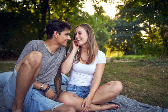 Young couple sitting in park, sharing earphones, listening music