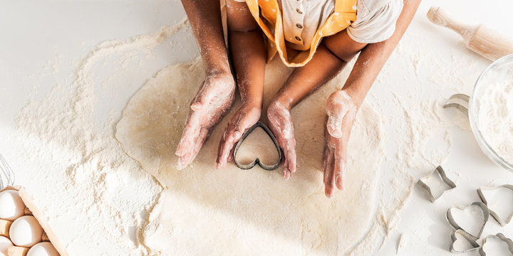 cropped image of african american mother and daughter preparing cookies with heart shaped mold in kitchen - Powered by Adobe