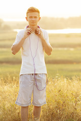 teenager in headphones listening to music on nature, young blond man looking straight on the background of beautiful summer landscape
