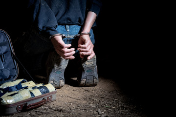 Drug dealer under arrest confined with handcuffs and hands at his back, standing next to a wall....