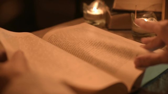 Big Close-up girl magician in a dark room with candlelight looking for a spell in a book. Low key live camera. Mystic. Small DOF