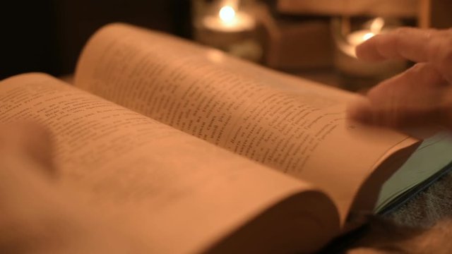 Big Close-up girl magician in a dark room with candlelight looking for a spell in a book. Low key live camera. Mystic. Small DOF