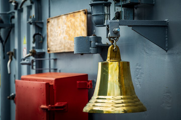 gilded old bell hanging aboard a warship. yellow bell on a warship.