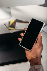cropped view of african american female businesswoman holding coffee to go and smartphone with blank screen