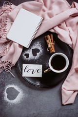 Valentines day. Cup of coffee, notebook, scarf, cinnamon and heart on gray table from above in flat lay style.