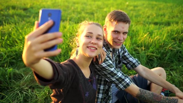 A guy and a girl sit on the grass and take selfies. Couple on a picnic doing a selfie. People in love look at the phone and smile.Friends fooling around in front of the camera.The lovers posing.