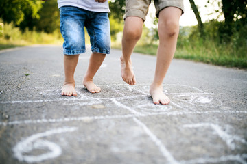 Two small boys hopscotching on a road in park on a summer day.