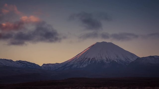 Perfect cone of volcano Mt Doom in New Zealand lit by rising sun in the early winter morning. Tongariro National Park, popular tourist destination and home to several volcanos. Timelapse video.