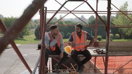 People working in construction site. Two happy men laughing at work in new house inside apartment building. Team of workers smoking cigarette and talking during break