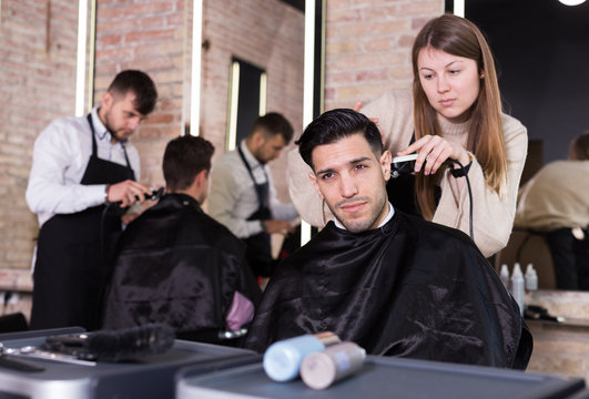 Hairdresser cutting hair of male with electric clipper