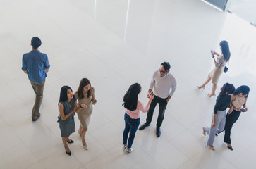 Asian office workers stand and talk in the office lobby.