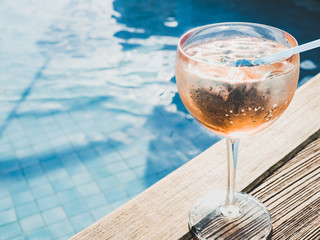 Beautiful glass with a pink cocktail and ice cubes on the background of the pool with blue water....
