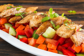 Tilapia fish fillet roasted in olive oil and served with fresh vegetable salad in white dish on wooden rustic table, closeup