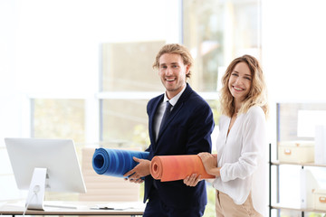 Young businessman and businesswoman holding yoga mats in office. Gym after work