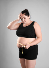 Fototapeta na wymiar Fat woman with measuring tape on grey background. Weight loss