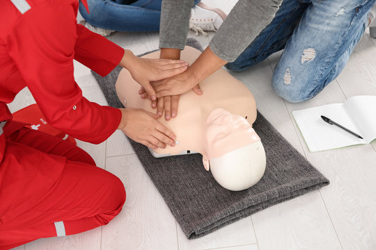 Group of people with instructor practicing CPR on mannequin at first aid class indoors, closeup