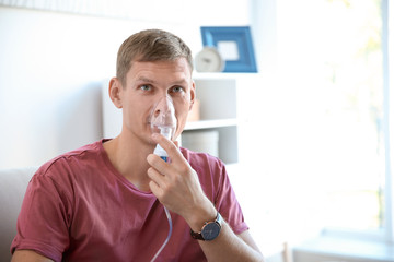 Young man using asthma machine indoors. Space for text