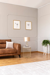 Real photo of an elegant living room interior with a brown sofa and lamp in a tenement house