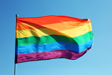 Rainbow LGBT flag fluttering on blue sky background. Gay rights movement