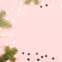 Christmas background with fir branches, Christmas lights and confetti on pink background. Copy space