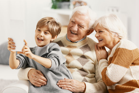 Happy seniors sitting on the couch in living room, posing for a photo with their teenage grandson