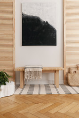 Black and white abstract painting above wooden table in natural designed interior with wooden screens and carpet on parquet floor