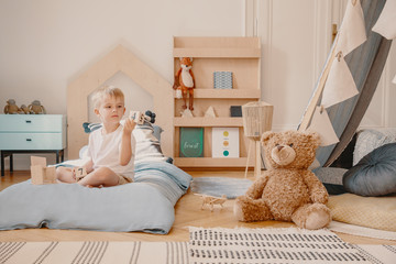 Teddy bear next to boy on blue bed in scandinavian bedroom interior with wooden furniture. Real...