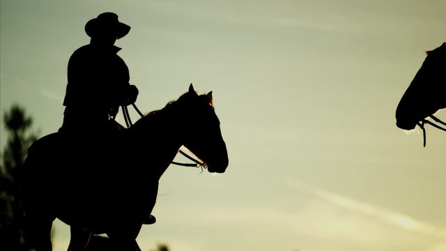 Silhouette at sunrise of cowboy riders in forest wilderness area of Canada