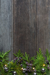 Christmas decoration thuja branches, LED lights and little bells placed on dark old wooden boards with space for text