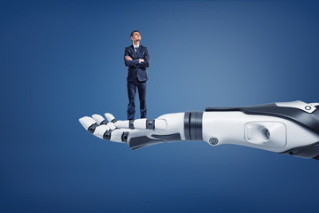 A small thinking businessman looks up while standing on a huge robotic arm.