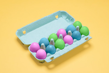 Dozen dyed easter eggs in carton container.  Pastel painted easter eggs in egg crate on a bright pastel yellow background with copy space and room for text