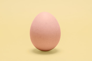 Single organic brown egg standing up on a yellow background.  Center composition with copy space...