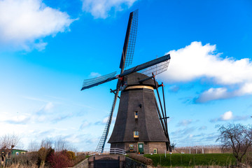Traditional dutch windmill near the canal. Netherlands. Old windmill stands on the banks of the canal, and water pumps. White clouds on a blue sky, the wind is blowing.