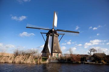 Old, traditional windmill in the Dutch canals. Netherlands.White clouds on a blue sky, the wind is blowing.