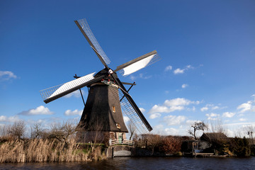 Fototapeta na wymiar Old, traditional windmill in the Dutch canals. Netherlands.White clouds on a blue sky, the wind is blowing.