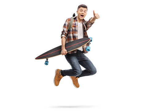 Teenage boy with a backpack and a longboard jumping and holding his thumb up