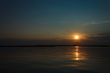 Sunset on the lake. Evening sky with beautiful clouds is reflected in the water of the lake
