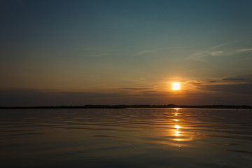 Sunset on the lake. Evening sky with beautiful clouds is reflected in the water of the lake