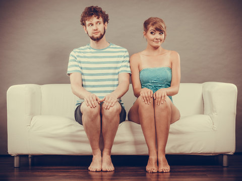 Shy woman and man sitting close to each other on couch.