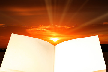An open book with a sunrise in the background at sea