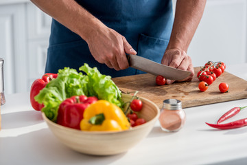 partial view of man cutting cherry tomatoes on cutting board on the kitchen