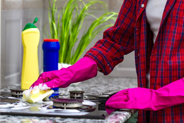 Housewife in colored rubber gloves washes a gas stove with detergent in the kitchen. House cleaning