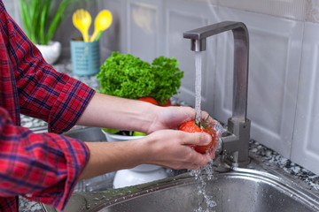 Woman washing vegetables in the kitchen at home. Fresh vegetables for salad. Healthy and right food, proper nutrition. Homemade food concept.