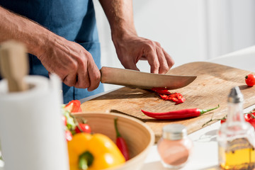 close up view of male hands cutting chili peppers on chopping board