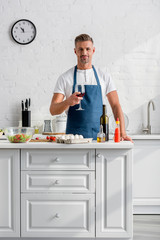 man with glass of wine in hand and different products on kitchen table